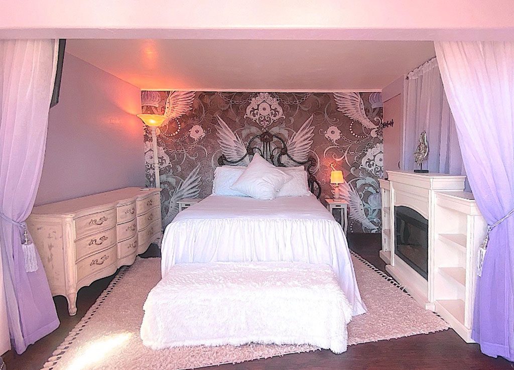 A bedroom with a bed, dresser and fireplace.